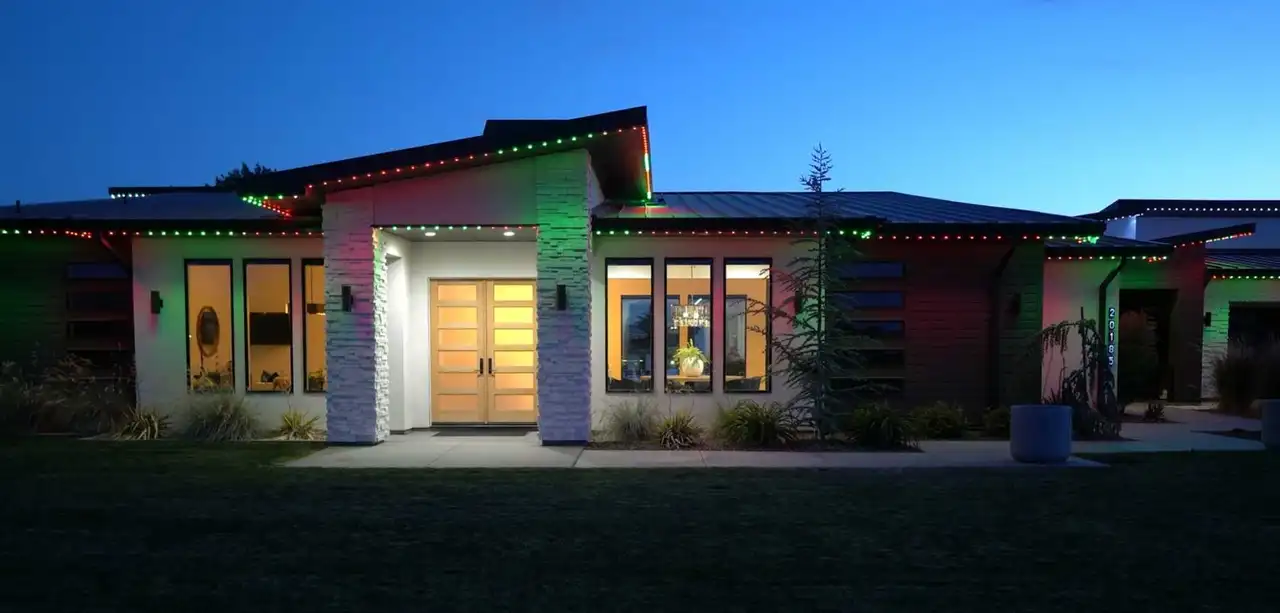 Modern single-story home at dusk with red and green permanent lighting along the rooflines