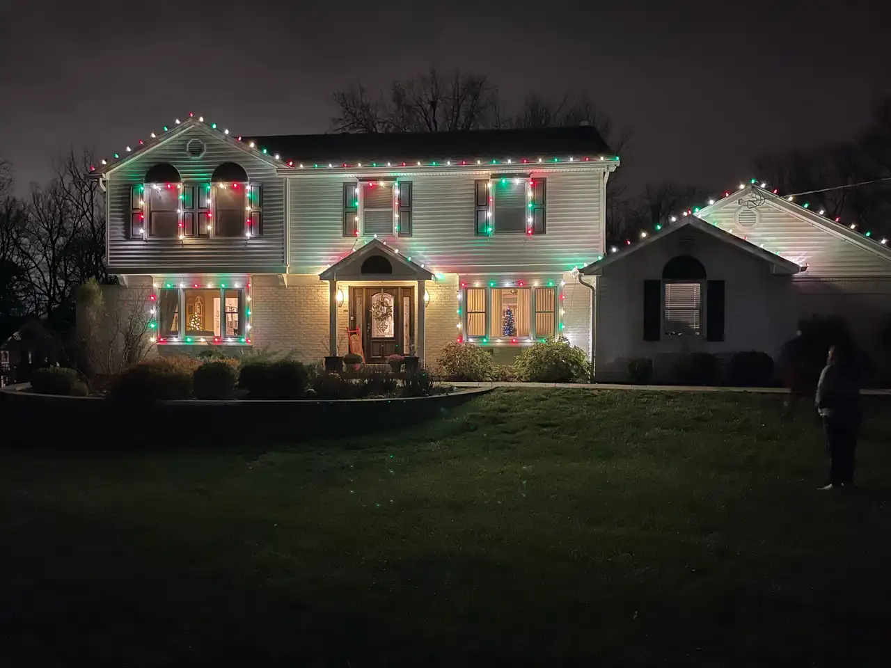 Two-story home in the Cincinnati area at night with red, green and white Christmas lights on the rooflines and around the windows
