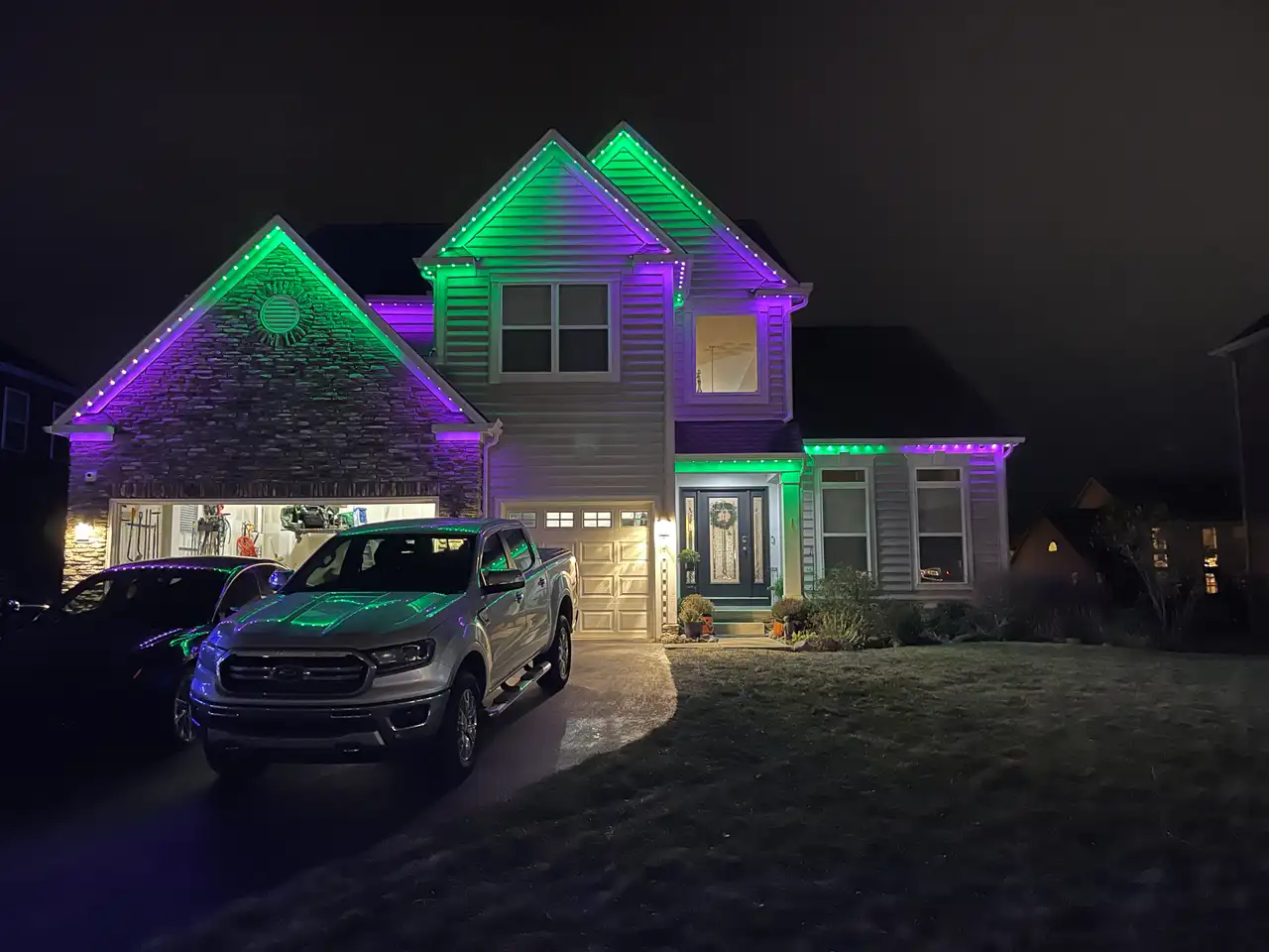 Two-story home in Cincinnati, OH at night with purple and green permanent LED lighting along the gables and rooflines
