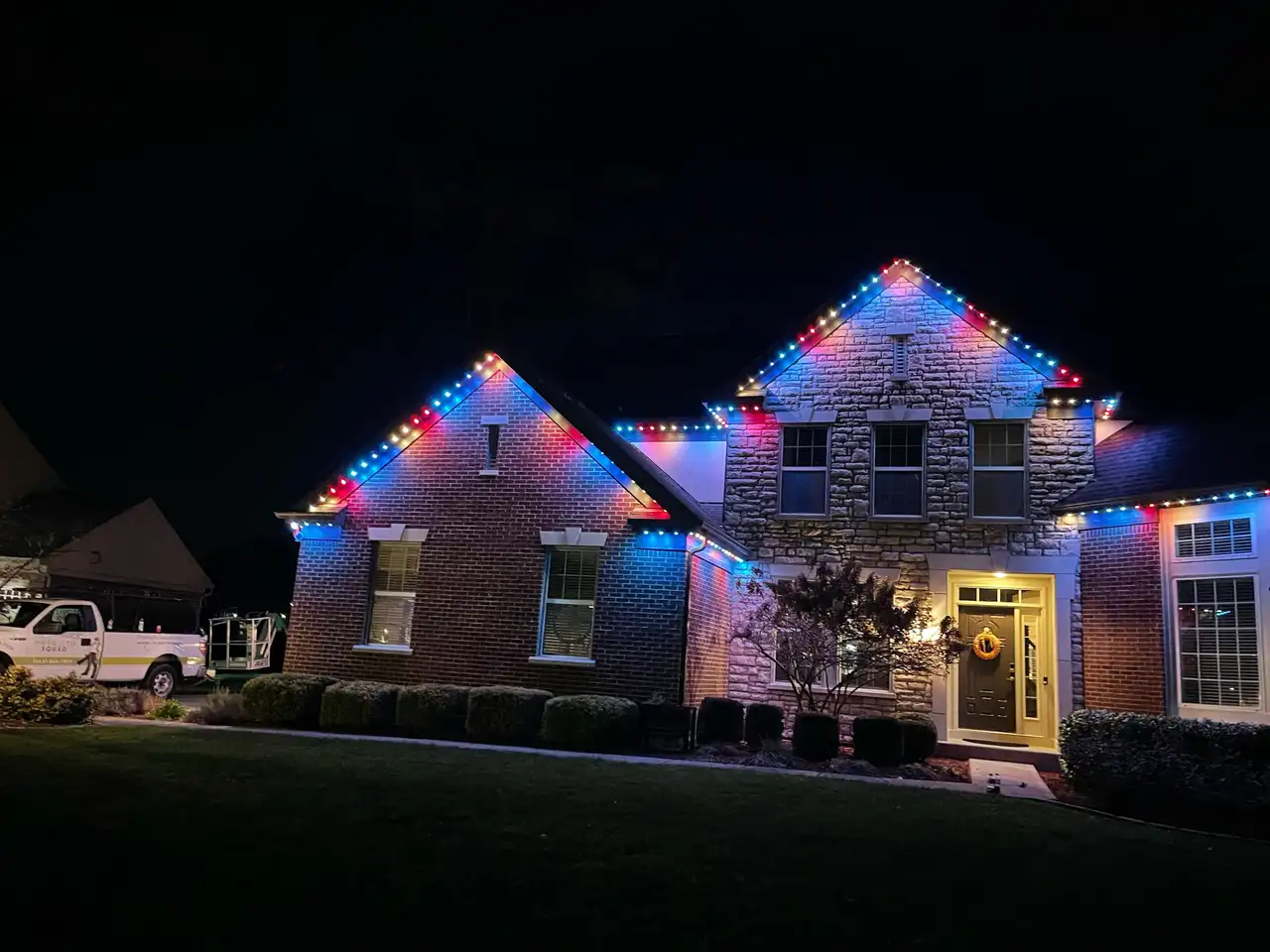 Brick and stone home in Mason, Ohio at night with red, white and blue permanent LED lighting along the rooflines