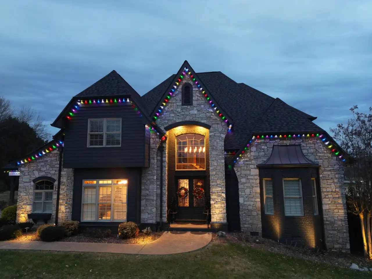 Stone and dark-sided home in the Chattanooga area at dusk with multicolor roofline lights and warm uplighting on the stone