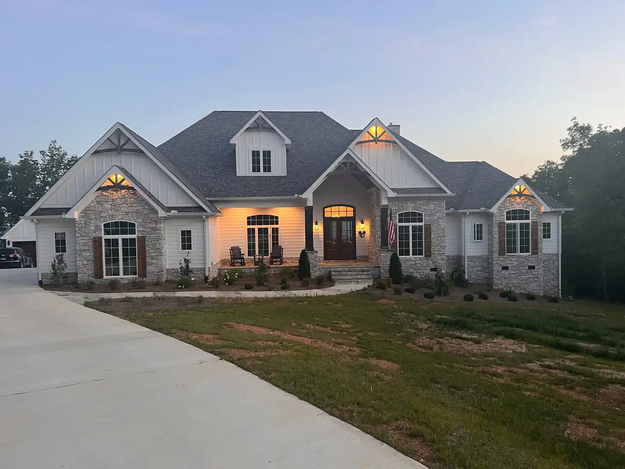 White and stone home in Jasper Highlands, near Chattanooga, at dusk with soft white accent lighting in the gables and on the front porch