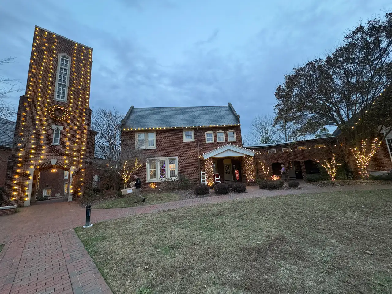 Brick tower and buildings at Baylor School in Chattanooga at dusk, outlined in warm white holiday lights with a lit wreath on the tower
