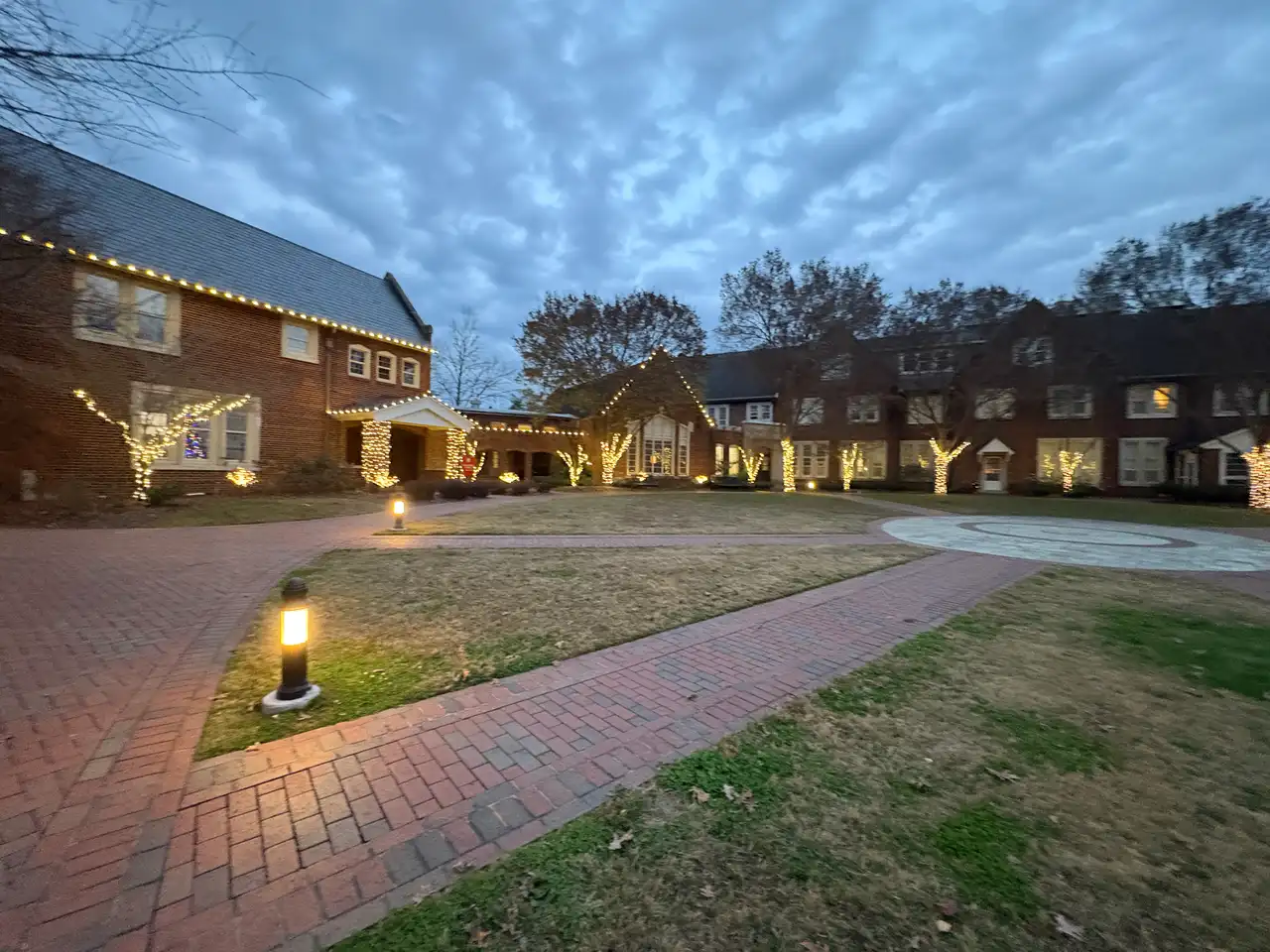 Courtyard at Baylor School in Chattanooga at dusk with warm white holiday lights along the rooflines and on wrapped trees and columns