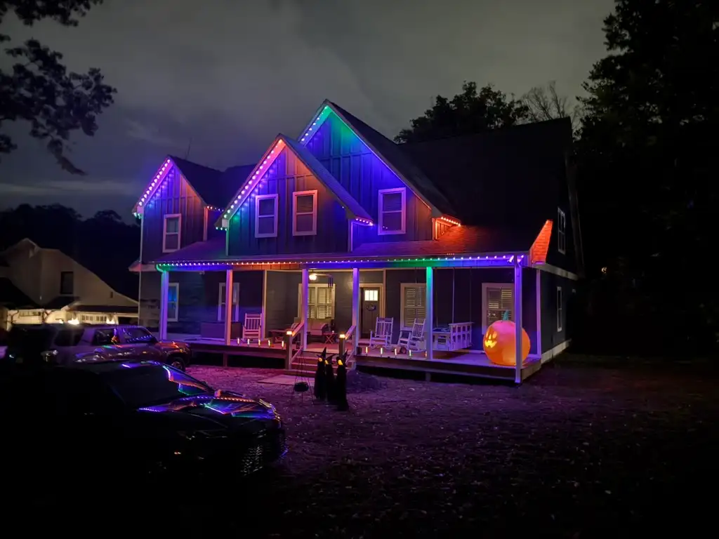 Home in Shoal Creek, AL at night with purple, blue and green permanent LED lighting along the gables and porch, with Halloween decorations in the yard