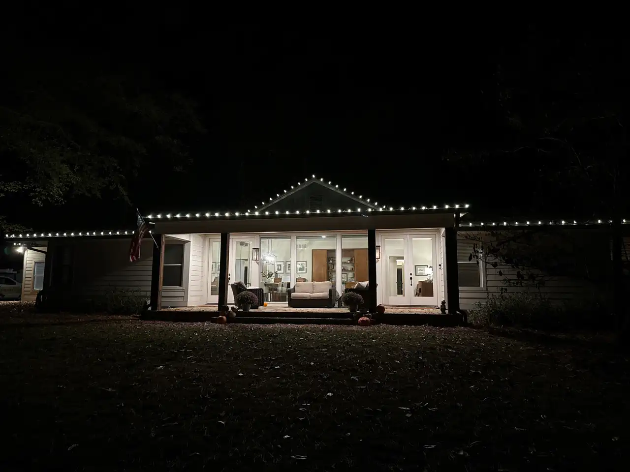 White ranch home in the Birmingham area at night with warm white lights along the roofline and porch gable