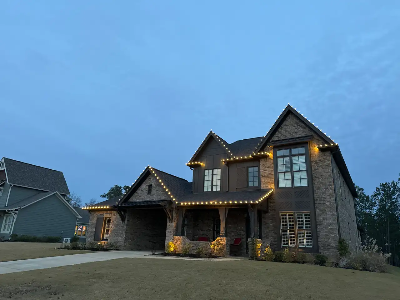 Brick home in the Birmingham area at dusk with warm white lights outlining the gables and rooflines