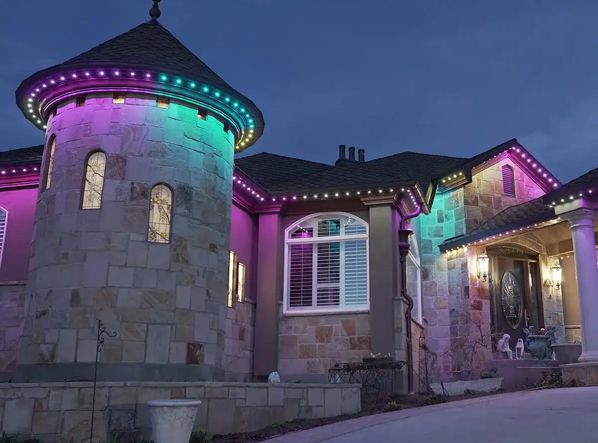 Stone home with a turret at dusk with pink and teal permanent lighting along the rooflines